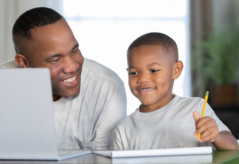 Man works with young student, smiling at laptop, pencil in hand