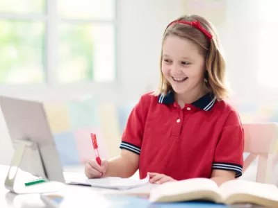 A girl sitting at a table with a laptop, writing something down
