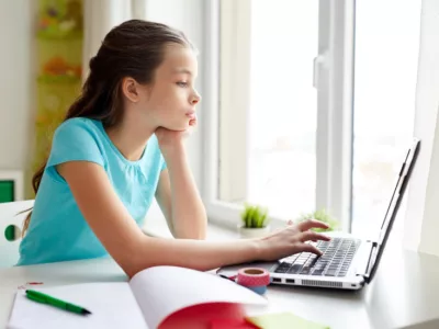 Girl works on laptop near a bright window
