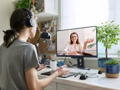 Student wearing headphones converses with teacher over video chat
