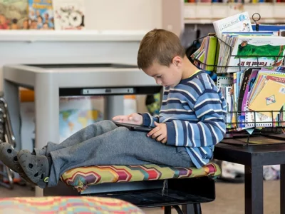 Student sits inside classroom, looking down at book and reading alone
