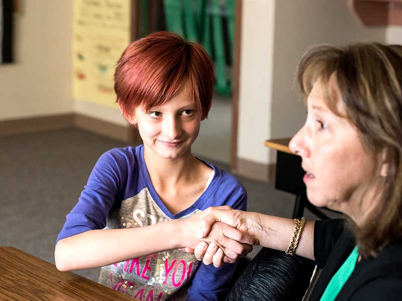 Female student looks at adult woman while shaking her hand