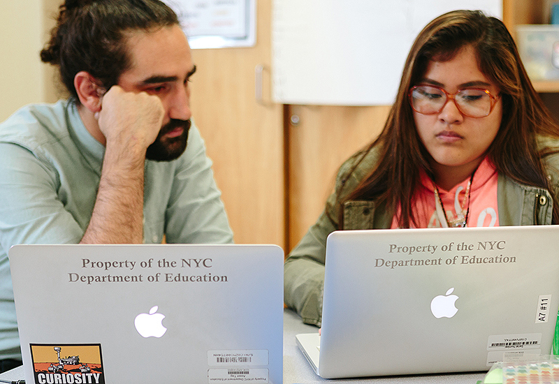 Teacher and student speaking, working on laptops