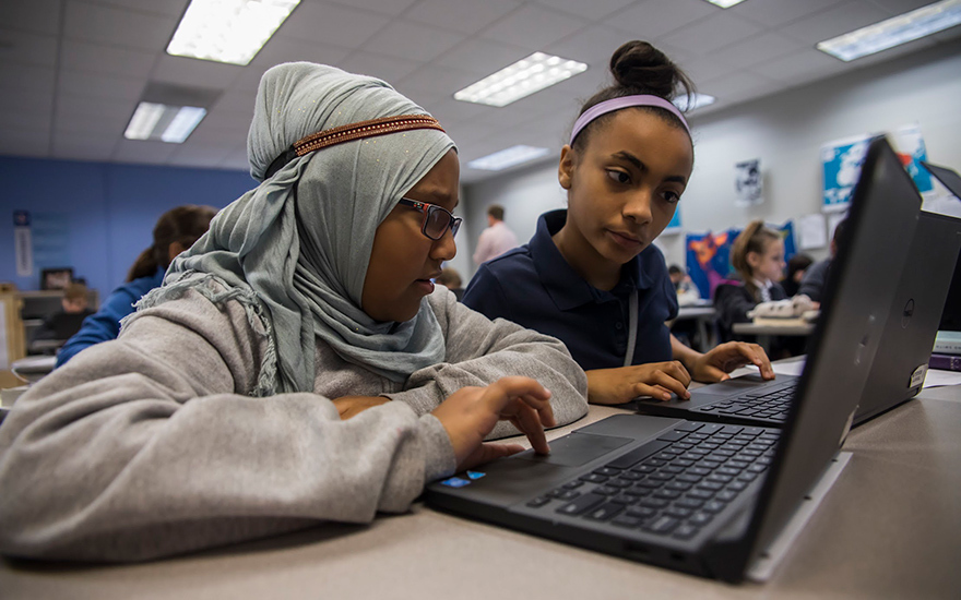 Two students looking closely at the same laptop