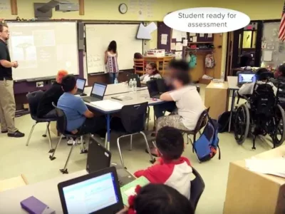 Photo of classroom with indication showing student is signing up for assessment on the whiteboard at front of class
