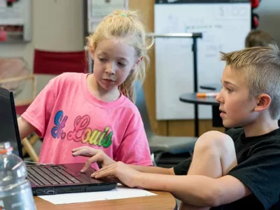 Male student sits at laptop while female student looks on from the side
