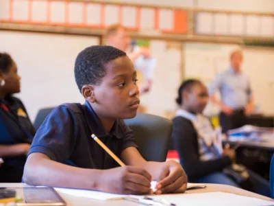 Student sits in classroom, looking off to the side as he holds a pencil
