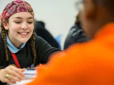 Student looks on with other student at papers on desk
