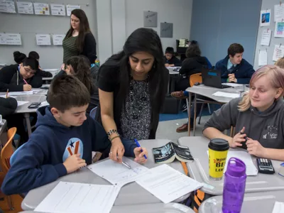 One teacher works with one group of students as another teacher in the background works with other students
