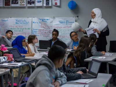 Teacher holds pen and speaks to class as students listen

