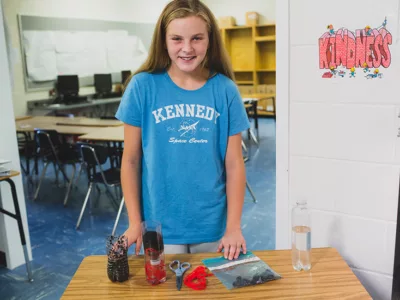 Student smiles for photo, standing in front of table with experiment materials
