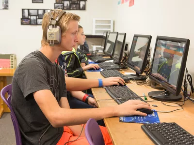 Students sit in row at computers, looking at screens
