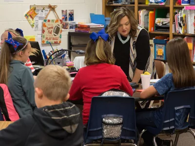 Teacher speaks with four students in a group at one table
