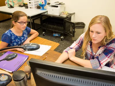 Teacher and student look on at computer screen
