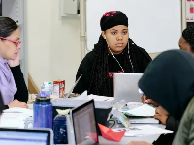Student looks closely at another person at desk

