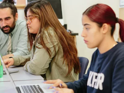 Two students and teacher look at laptops
