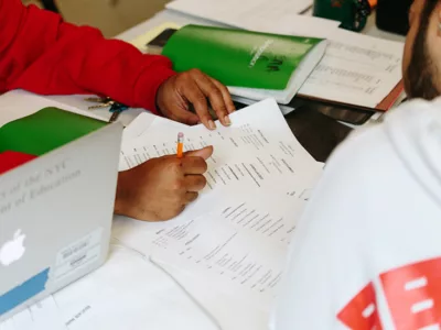 Overhead view of person writing on paper while another looks on
