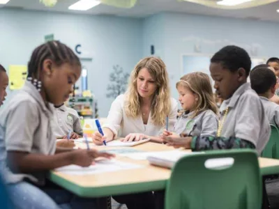 Photo of teacher working with a group of students at table in classroom
