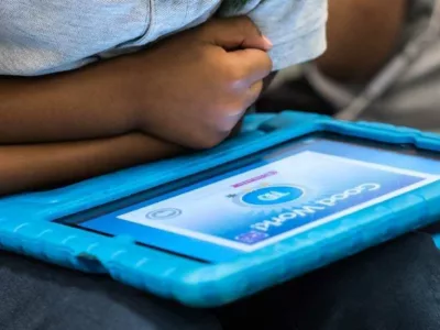 Photo closeup of tablet screen reading "Good Work" with student in background
