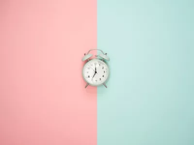 Alarm clock sitting on top of a two-toned pink and turquoise background

