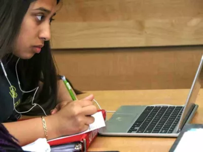Photo of student working on her laptop and writing by hand
