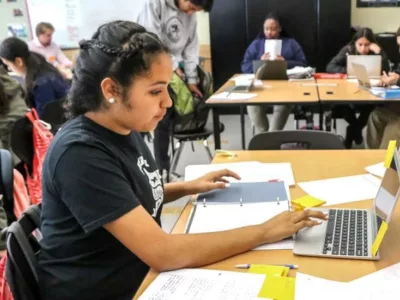 Photo of seated student working with her notebook and on her laptop
