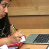 Photo of student working on her laptop and writing by hand
